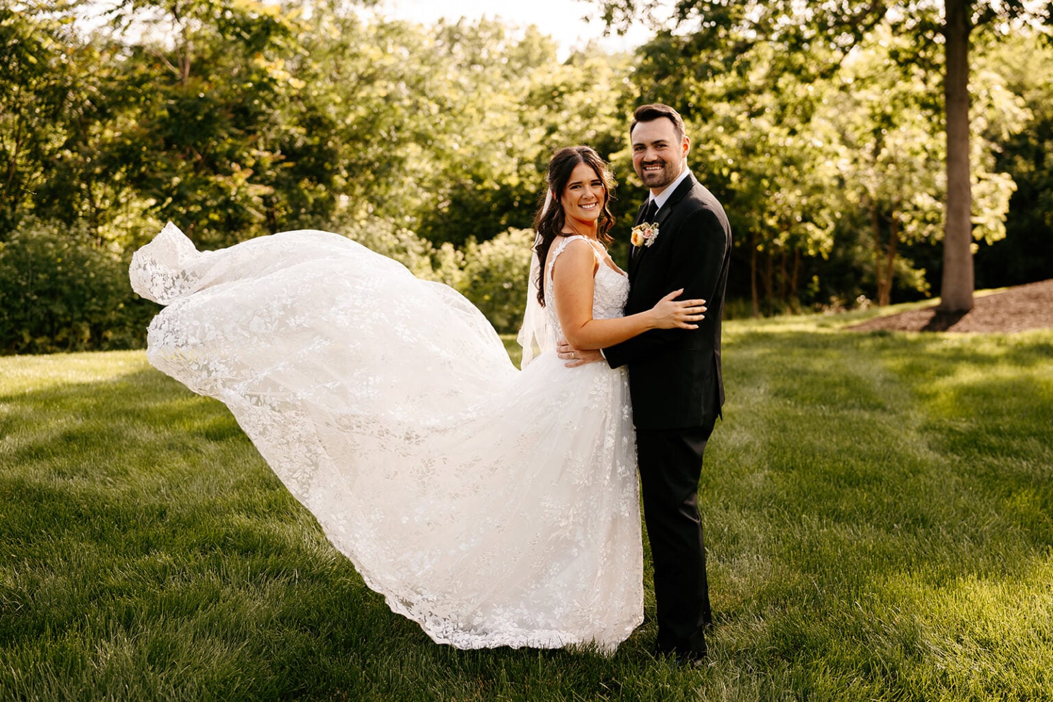 Rachel and Jackson smile together on the lawn as the lace skirt of Rachel’s wedding dress lifts in the breeze.